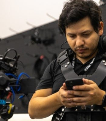 Alex, Pixel Studio Productions videographer, on set wearing a camera rig and checking his phone